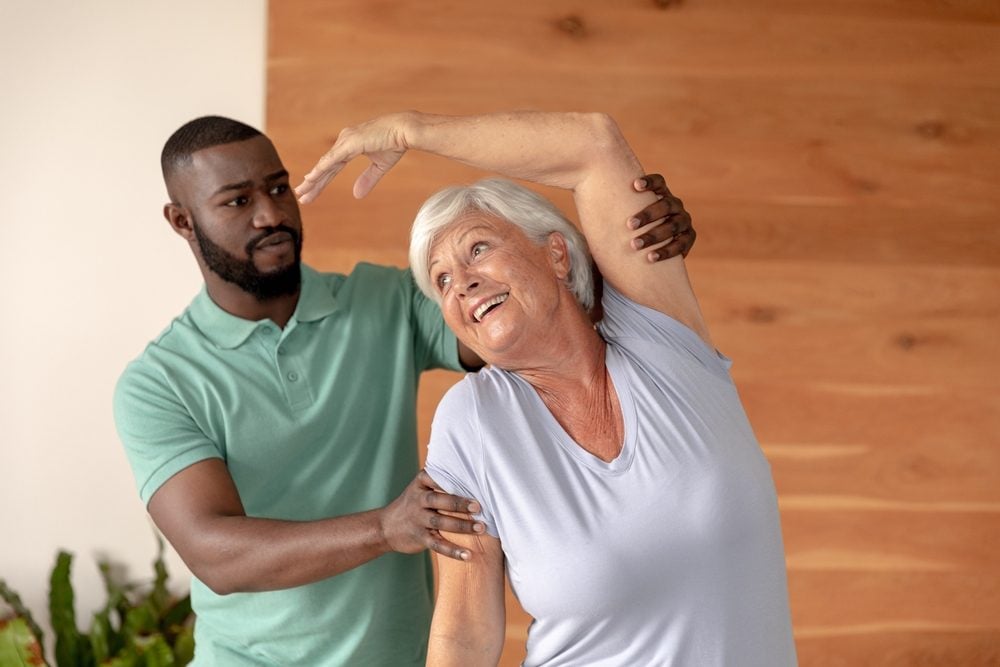 African,American,Male,Physiotherapist,Helping,Caucasian,Senior,Woman,To,Stretch